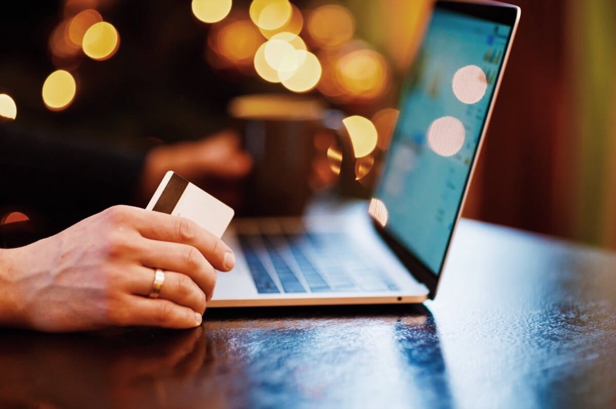 Création de site e-commerce 1 Main tenant une carte bancaire devant un ordinateur portable illustrant la création de site e-commerce avec fonctionnalité de paiement en ligne